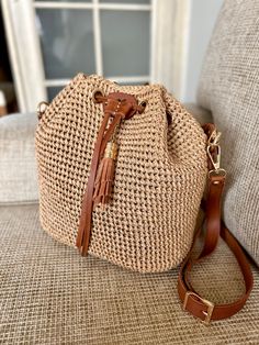 a straw bag sitting on top of a couch next to a window with a brown leather strap