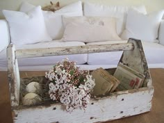 an old wooden box with books and flowers in it sitting on the floor next to a couch