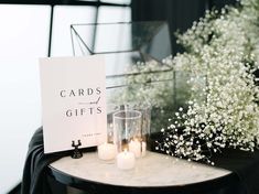 two candles are sitting on a table next to a card and vase with baby's breath flowers