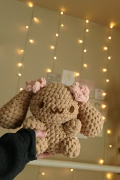 a small crocheted stuffed animal being held up by someone's hand with lights in the background