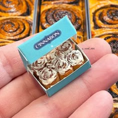 a hand is holding a tiny box of cinnamon rolls with icing on top and the inside of it