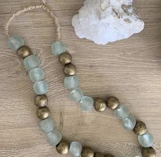 a necklace with gold and aqua glass beads on a wooden table next to a rock