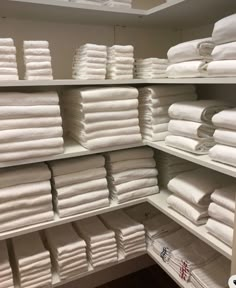 the shelves are filled with white towels and folded ones in rows, all stacked on top of each other