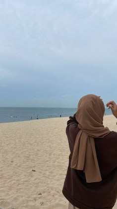 a woman standing on top of a sandy beach next to the ocean wearing a brown shawl