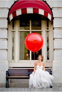 a woman sitting on a bench in front of a building with a red balloon attached to it