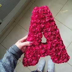 a person holding up a letter made out of red flowers in front of their feet