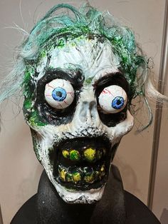 a creepy mask with green hair and blue eyes on top of a mannequin's head