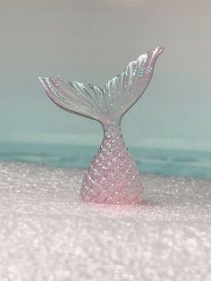 a small glass mermaid tail sitting in the sand