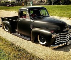 an old black truck is parked on the side of the road