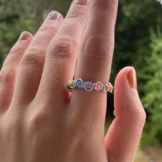 a woman's hand with an open ring on it and trees in the background