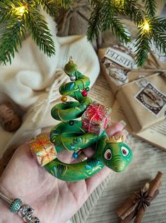 a hand holding a small christmas tree ornament in it's palm, surrounded by other holiday decorations