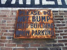 a rusted sign on the side of a brick building that says please do not bump into building when parking