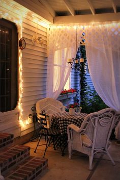 an outdoor patio covered in white curtains and string lights, with wicker furniture on the front porch