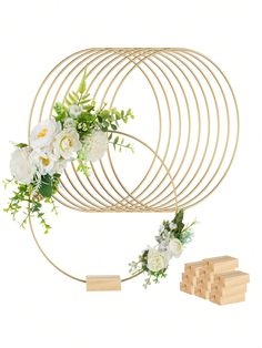 an arrangement of flowers and greenery is arranged on a gold wire sculpture with wooden blocks