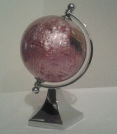 a pink and white globe sitting on top of a metal stand next to a wall