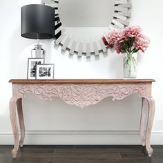 a pink console table in front of a mirror and vase with flowers on the top