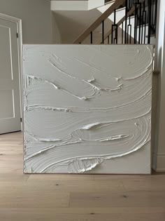 a white painting sitting on top of a hard wood floor next to a stair case