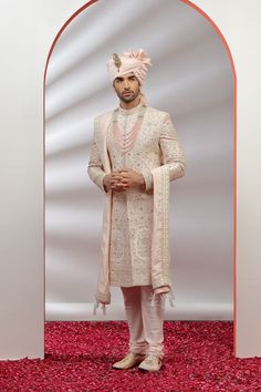 a man standing in front of a mirror wearing a white suit and pink turban