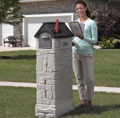 a woman standing next to a mailbox in front of a house holding a book