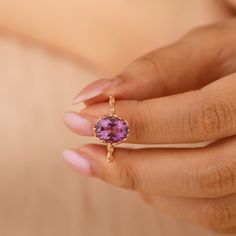 a woman's hand holding a ring with a pink stone