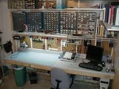 a computer desk with lots of electronics on top of it in a room filled with books