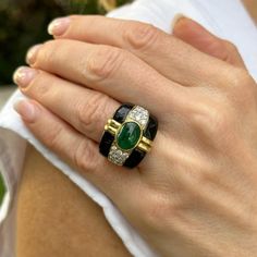 Fabulous emerald, diamond, and onyx cocktail ring handcrafted in 18 karat yellow gold. The band features a bezel set oval cabochon green emerald weighing approximately 4.00 carats, 24 round briliant cut diamonds weighing approximately 2.50 carat total weight, and onyx accent. The diamonds are graded H-I color and SI clarity. The ring measures 19.5mm in width tapering down to 6.5mm, and is currently size 8.5 (can be sized). Weight: 18.4 grams. Luxury Emerald Ring With Oval Cabochon And 17 Jewels, Luxury Oval Cabochon Emerald Ring With 17 Jewels, Luxury Emerald Ring With Oval Cabochon, Luxury Oval Cabochon Emerald Ring, Luxury Green Cabochons, Elegant Oval Black Enamel Ring, Luxury Oval Emerald Ring With Bezel Setting, Designer Oval Gemstone Rings, Elegant Emerald Ring With Oval Cabochon Bezel Setting