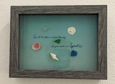 some sea glass in a shadow frame on the wall with a quote written below it