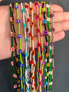 a hand holding several bracelets with beads and flowers on each beaded strander