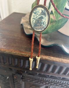 This awesome bolo tie has a vintage fox print with a clear resin coating and metal backing. Handmade in our shop!The cord is brown and made of genuine woven leather.Our bolos pair nicely with many of our belt buckles! They make wonderful gifts.The western bolo tie rope length is 39'' ; pendant size is 1 1/2'' x 1 1/4'' Vintage Adjustable Hand Tooled Bolo Tie, Vintage Brown Jewelry For Rodeo, Adjustable Vintage Hand Tooled Bolo Tie, Vintage Brown Jewelry For Western-themed Events, Vintage Adjustable Jewelry For Western-themed Events, Retro Adjustable Brown Jewelry, Retro Brown Adjustable Jewelry, Vintage Brown Bolo Tie With Adjustable Length, Adjustable Vintage Brown Jewelry Gift