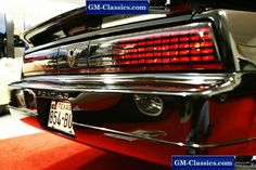 the rear end of an old car that is parked in a garage with red carpet