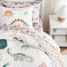 a white bed topped with pillows next to a night stand and lamp on top of a wooden floor