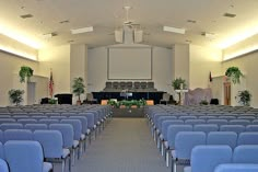 an empty church with rows of blue chairs in front of the alter and podiums