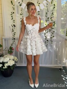 a woman standing in front of a window wearing a white dress with flowers on it