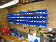 a workbench with many blue bins and tools hanging on the wall next to it