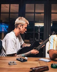 two men sitting at a table with guitars in front of them, one playing the guitar