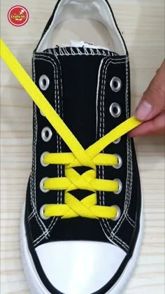 someone is tying the shoelaces to their black and white sneakers with yellow string