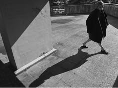 a woman walking down a sidewalk next to a cement structure with graffiti on it's side