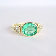 Item Details: 2.43 ct. natural Colombian Emerald vibrant light green color. Six round brilliant-cut diamonds weighing 0.06 ct (F/VS) Two trillion-shaped diamonds weighing 0.82 ct. (E/VS) Set in 18K yellow gold This ring is made with a one-of-a-kind center stone. To create a similar ring email custom@berlingerrings.com. Enquire about this ring Design a custom piece with us Gia Certified Oval Green Diamond Ring, Green Oval Diamond Ring Fine Jewelry, Oval Tsavorite Diamond Ring In Green, Oval Green Tsavorite Diamond Ring, Green Oval Ring With Brilliant Cut, Green Oval Rings With Brilliant Cut, Green Oval Diamond Ring With Center Stone, Green Oval Diamond Ring, Green Emerald Oval Diamond Ring