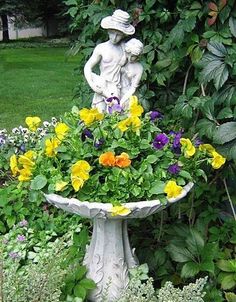 a bird bath with flowers in it and a statue next to the planter on the side