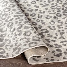 an animal print rug is laying on top of a wooden floor with a white and gray blanket