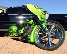 a green motorcycle is parked in front of a black pick - up truck with chrome rims