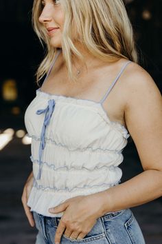 Head to the west(coast) in style with The Juliana Top. This cropped tank top features a charming cream color and playful ruffle details. The front bow adds a touch of cute cowgirl charm, perfect for a sunny summer day. Keasha is wearing size small paired with The Stacie Shorts Fitted Ruffle Hem Crop Top For Summer, Spring Sleeveless Tank Top For Picnic, Casual Ruffle Hem Crop Top For Spring, Casual Spring Crop Top With Ruffle Hem, Spring Tank Top With Tie Straps, Summer Tank Top With Tie Straps For Spring, Spring Vacation Crop Top With Ruffles, Summer Cotton Crop Top With Ruffled Straps, Cute Ruffled Tank Top For Spring