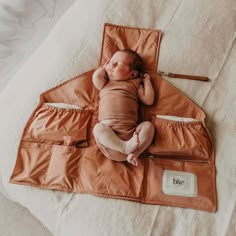 a baby is laying on top of an orange sleeping bag with its head resting on it's hands