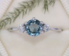 an engagement ring with a blue diamond surrounded by white diamonds and pine needles on a table