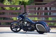 a black and blue motorcycle parked in front of a wooden fence on the side of a road