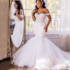 a woman in a white wedding dress looking at herself in the mirror with her hand on her hip