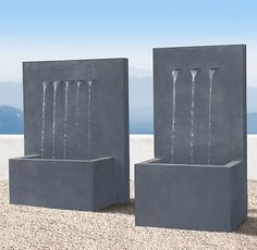 two cement water fountains sitting next to each other on top of a sandy ground with mountains in the background