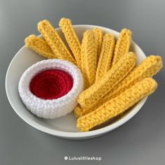 a white plate topped with yellow and red crocheted french fries next to a bowl of ketchup