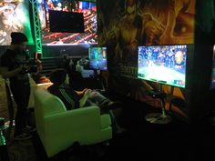 two people playing video games in front of large screen televisions at an indoor event