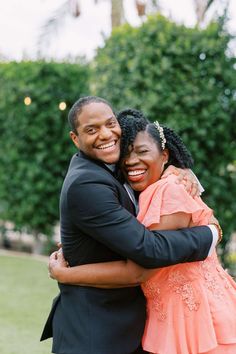 two people hugging each other in front of trees